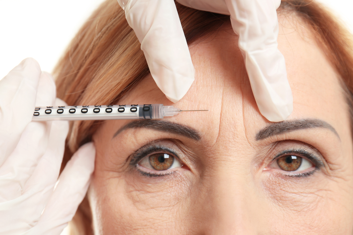 Dysport injections administered to forehead wrinkles of middle-aged woman by gloved medical professional.