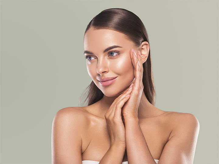 Fillers for volume loss highlighting woman with smooth, radiant skin touching her cheek in studio portrait.