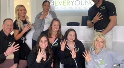 Eight 4Ever Young wellness clinic staff members in branded uniforms celebrating together in front of the illuminated clinic sign at a new location opening.