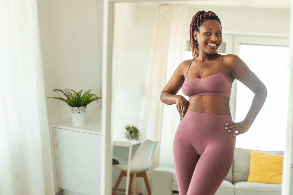 Tesofensine weight loss results depicted by a woman smiling confidently in athletic wear in front of a mirror.