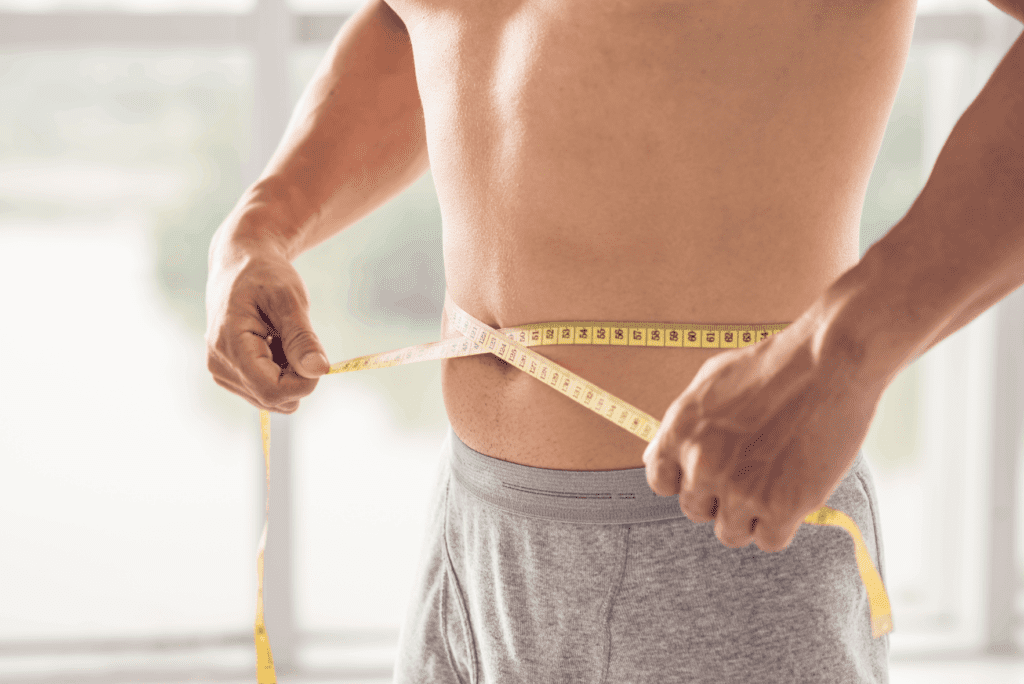 Man measuring his waistline, tracking progress from using weight loss medications.