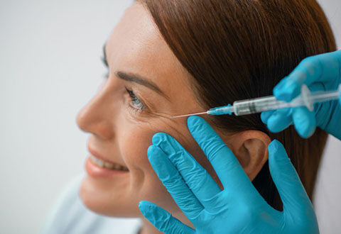 Practitioner injecting Botox into the crow's feet area of a smiling woman at a cosmetic clinic.