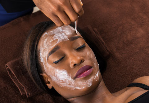 Aesthetician applying a white facial mask to a relaxed woman's face during a professional spa treatment.