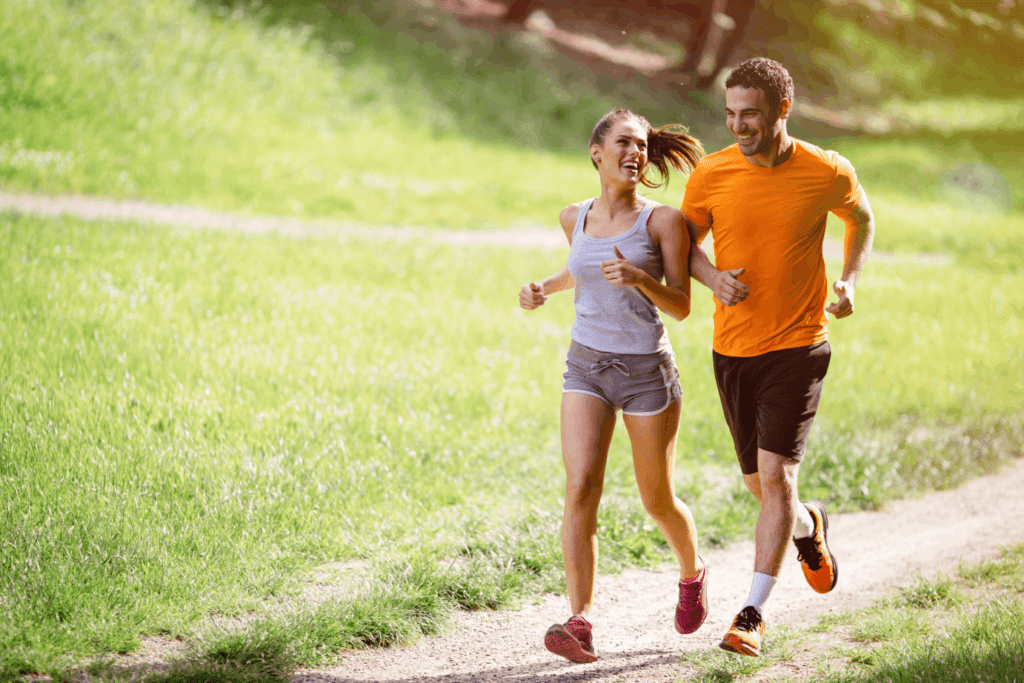 Prescription weight loss success shown by a fit couple jogging happily through a green park trail.