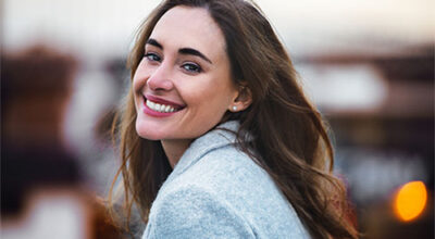 A smiling woman with glowing skin outdoors, reflecting the confidence that comes from targeted peptide therapy.