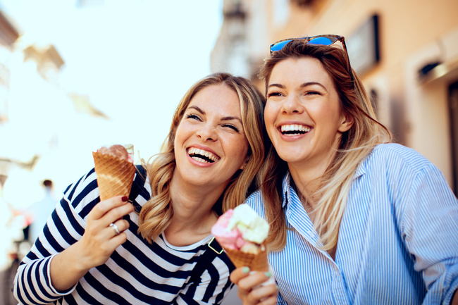 Metabolism-boosting medication results shown by two happy women enjoying ice cream and laughing outdoors.